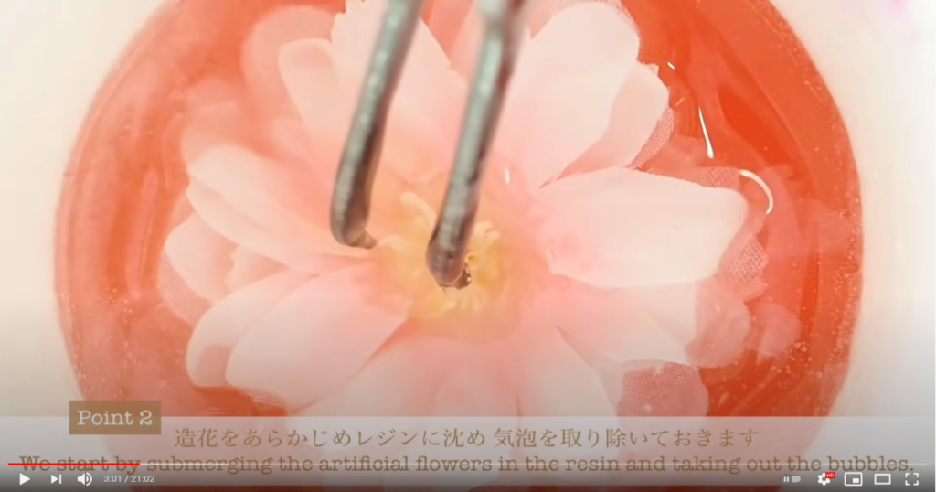 色付きレジンの中に造花を沈めて気泡を取り除いている様子とポイント2造花をあらかじめレジンに沈め気泡を取り除いておきますの文字