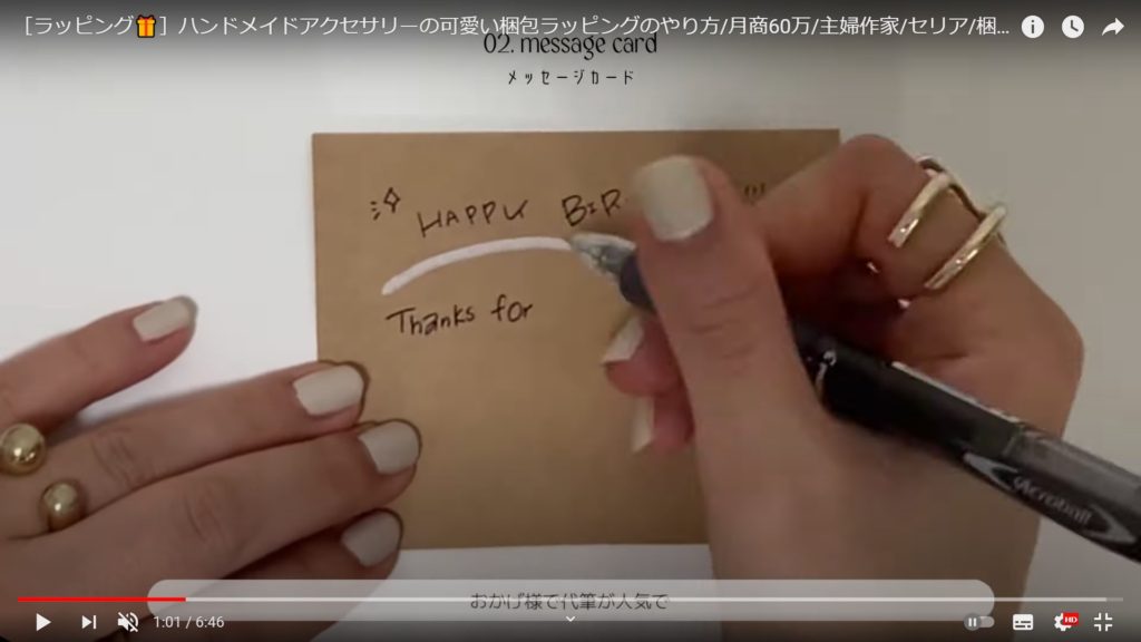 ペンを持ち茶色いカードに英字でメッセージをかく女性の手