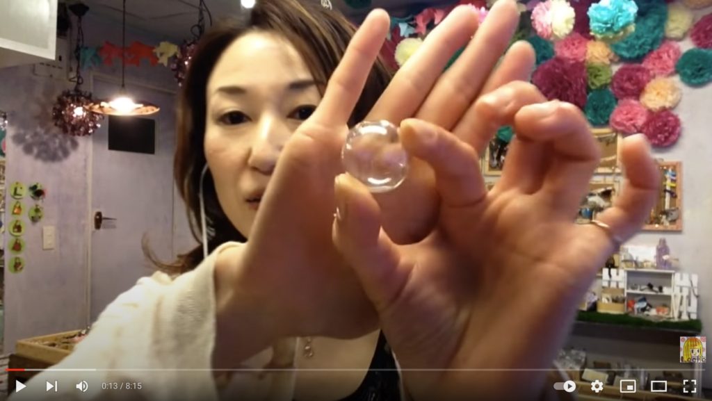 ヘアアクセサリーに使用するガラスドームを手に持ってガラスドームの大きさなどを紹介しているようすを写した写真。
