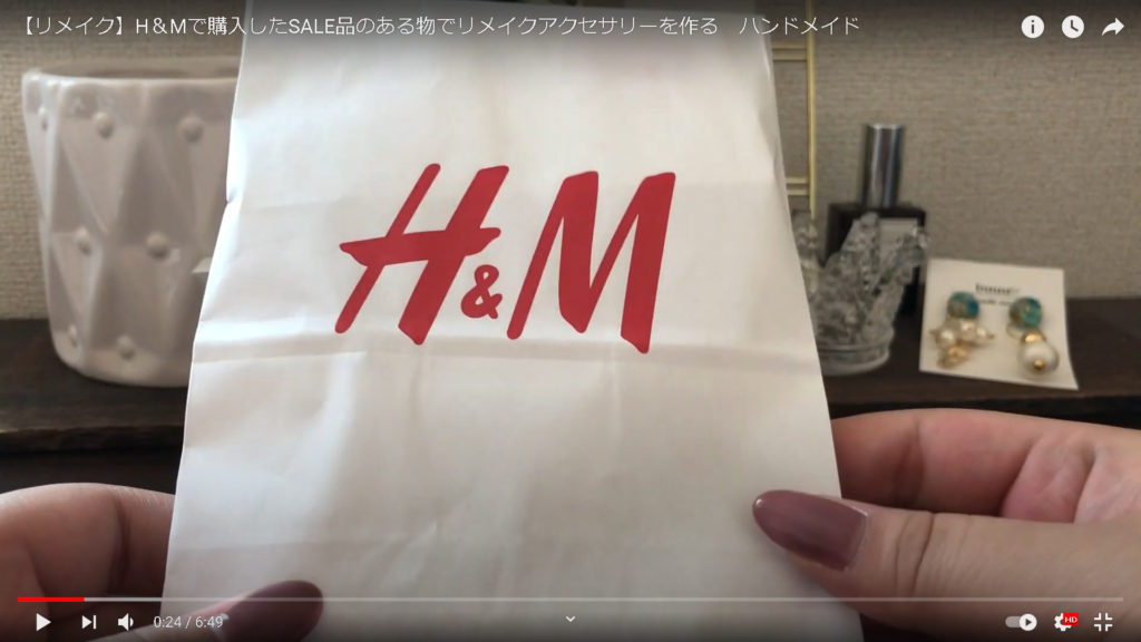 素材となるH＆Mのアクセサリーの入ったショップ袋を見せている場面です。
