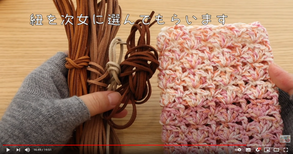 左手にスエード調の紐を、右手に編み終わってグラデーション上になった毛糸を持っている様子と紐を次女に選んでもらいますの字幕の画像