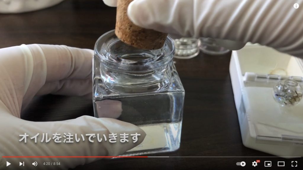 ハーバリウムオイルをガラスドームに注ぐために、オイルが入っているガラス瓶の蓋を開けているようすを写した写真。