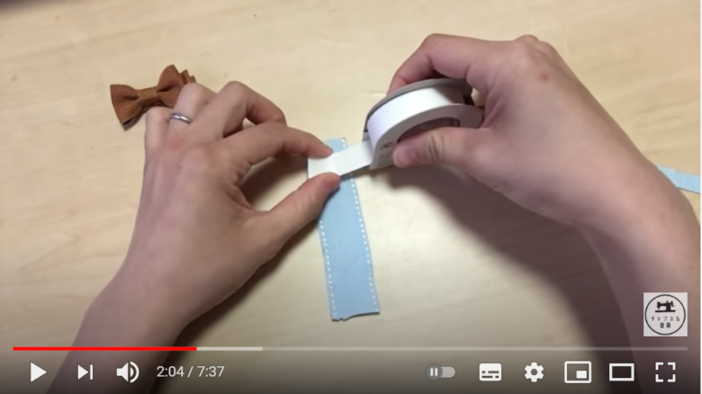 ヘアクリップを制作している場面。淡いブルーのリボンに、布用両面テープを貼り付けようとしている。