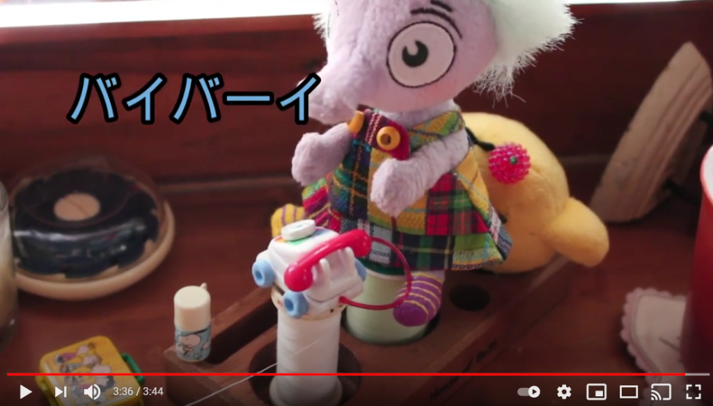 象の様なぬいぐるみがミシン糸の上に座っている。その前には、小さい電話の人形が置かれている。象の様なぬいぐるみの後ろには、ひよこのぬいぐるみが置かれている。