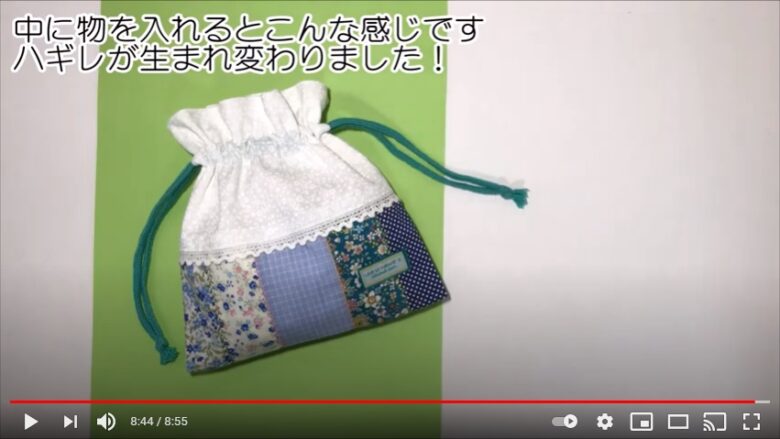 パッチワークした布と、白の花柄の布を使用した袋に緑の紐が通され、完成品を紹介する写真
