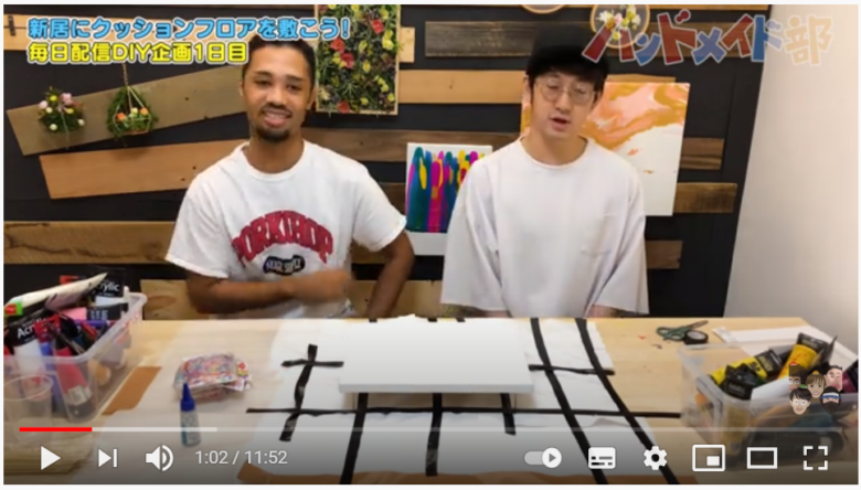 動画投稿者である「ハンドメイド部」の2人が、ポーリングアートのやり方を説明している場面。シンプルな木製のテーブルにキャンバスが置かれ、周囲には制作に必要と思われる画材等が用意されている。