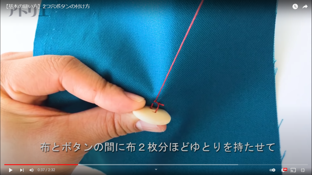 青色の生地に赤い糸を使って、2つ穴ボタンを縫い付けるときのポイントを解説しているシーン。