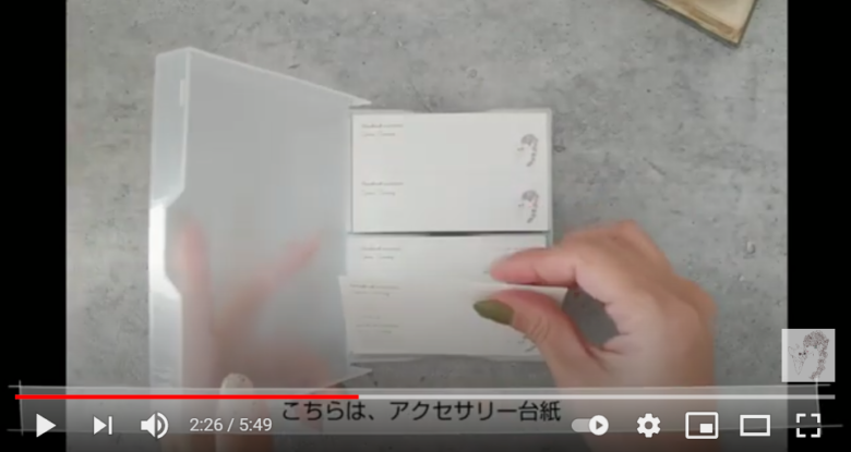 投稿者が実際に使用している、アクセサリーの台紙を公開している場面。台紙はカードケースに収められていて、名刺サイズで色は白。右にイラスト、左に作家名等が記載されている。