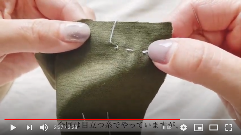 玉留めを行う布について話している場面。画面では深緑色の布に、白い糸で玉留めが施してある。