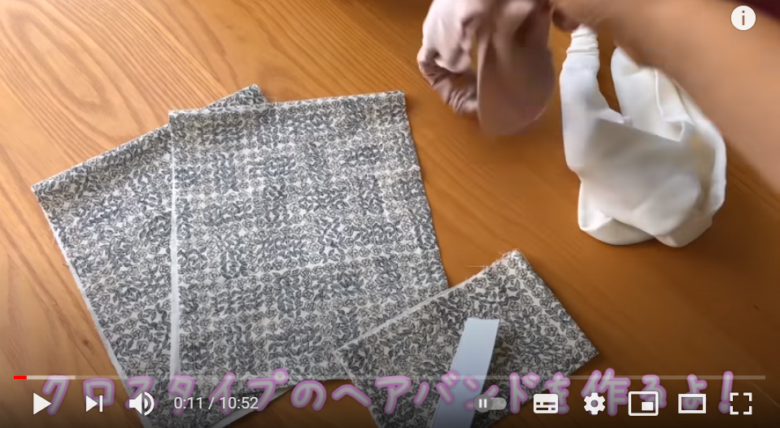 冒頭で、クロスタイプのヘアバンドの作り方を紹介する場面。テーブルにヘアバンドを作るための布が、それぞれのパーツにカットされた状態で置かれている様子が映り込んでいる。