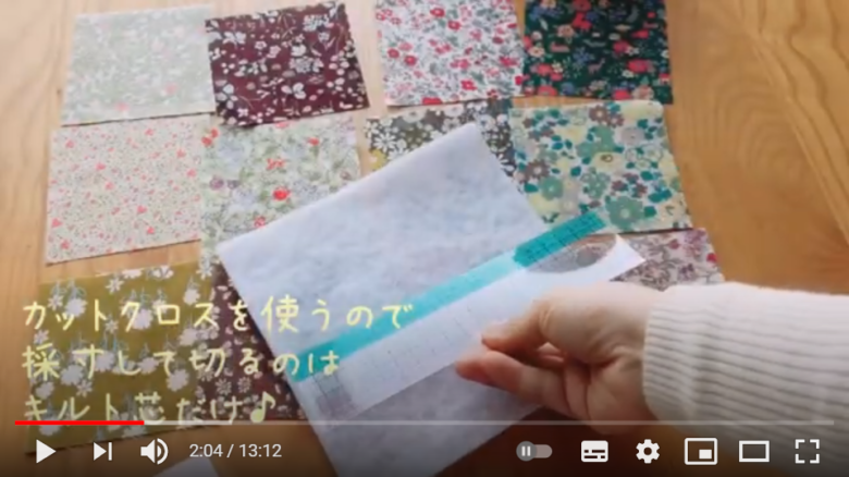カットクロスを使うので、生地を裁つ必要がないことを伝えている場面。並べられた12枚の生地の上にキルト芯が置かれ、カットするのはこれだけだということを併せて伝えている。