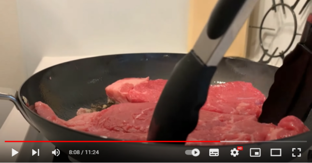 フライパンに2枚牛肉を入れて焼いている様子。投稿者さんはトングをもってお肉の位置を調整しています。