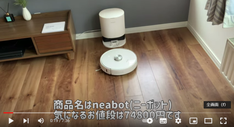部屋の一角に、ロボット掃除機が置かれている。本体は白く丸い。ホーム部分も白く、楕円形をしている。