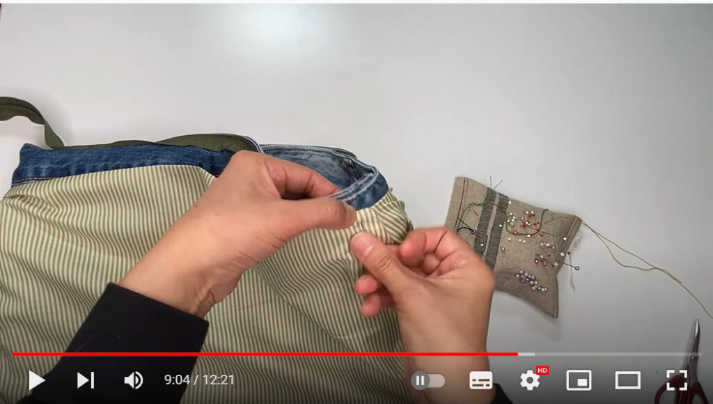 袋口の周りに内布を縫い付ける場面です。バッグの端を手で持ち、まち針で止めているところです。
