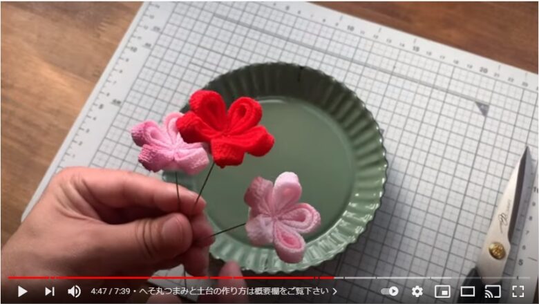 へそ丸つまみで作ったピンクのお花2個と赤のお花1個に土台とワイヤーが付き、ワイヤー部分を手で持っている写真