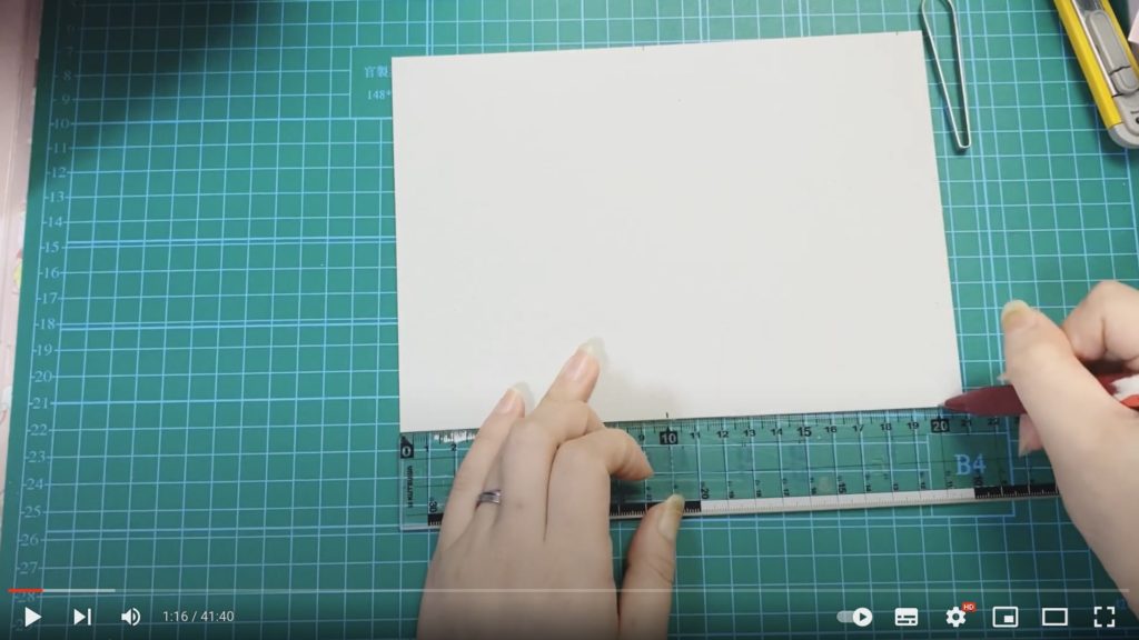 ボールペンと定規を使って、白い厚紙に寸法を記載している写真。左手に定規を持って、右手にボールペンを持っています。