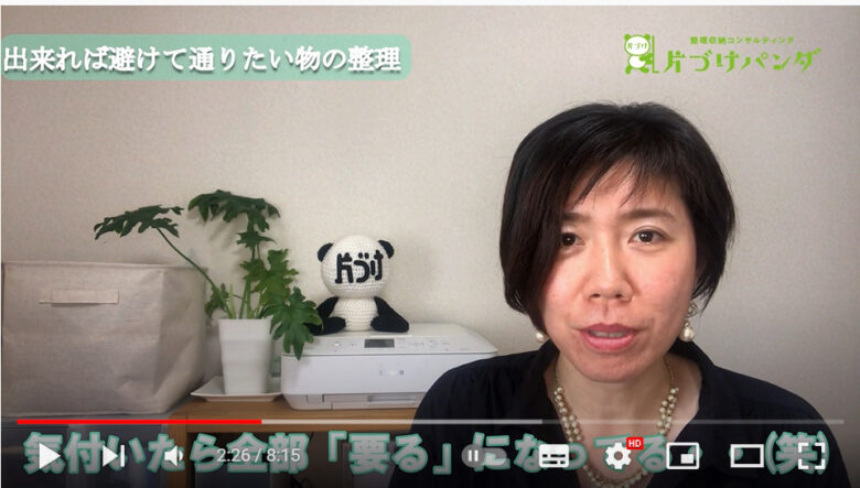 話をしている中村さんの写真です。後ろには顔に「片づけ」と書かれたパンダの編みぐるみが置かれています。