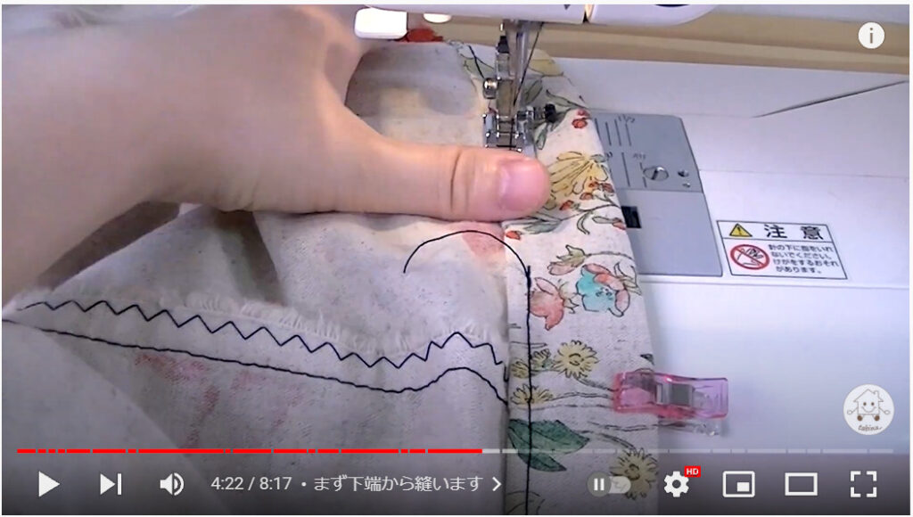 袋口をミシンで縫っている写真です。袋口を3つ折りし、左手でおさえて黒の糸で縫っています。右側は小さなクリップで止めています。