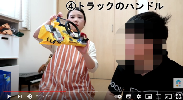 女性がトラックのハンドルの形をしたおもちゃをこちらに向けている。女性の左側には息子さんが座っている。
