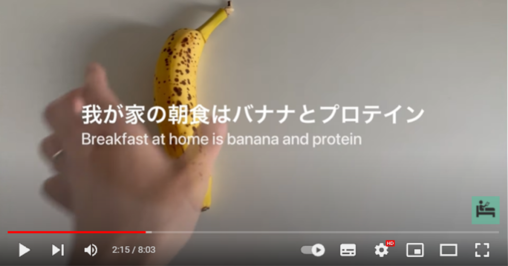 テーブルにバナナを置いている様子を映した場面で、画面のテロップには「我が家の朝食はバナナとプロテイン」と表示されています。