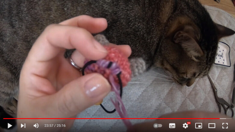 完成した猫の編みぐるみの後ろにヘアゴムを縫い付けている様子