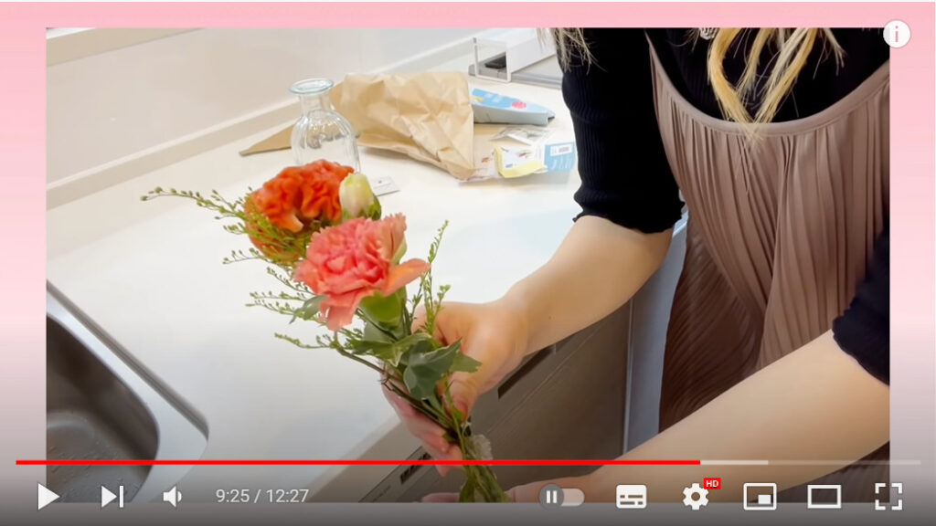 投稿者がキッチンで花束をこちらに見せている写真です。淡いサーモンピンクのカーネーションが素敵です。