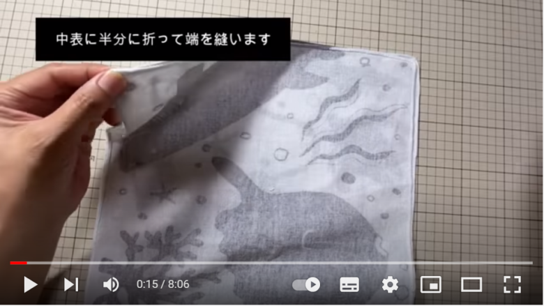 動画の冒頭部分にて、魚のイラストが入ったの手ぬぐいを中表に合わせ、縫い合わせようとしている場面。