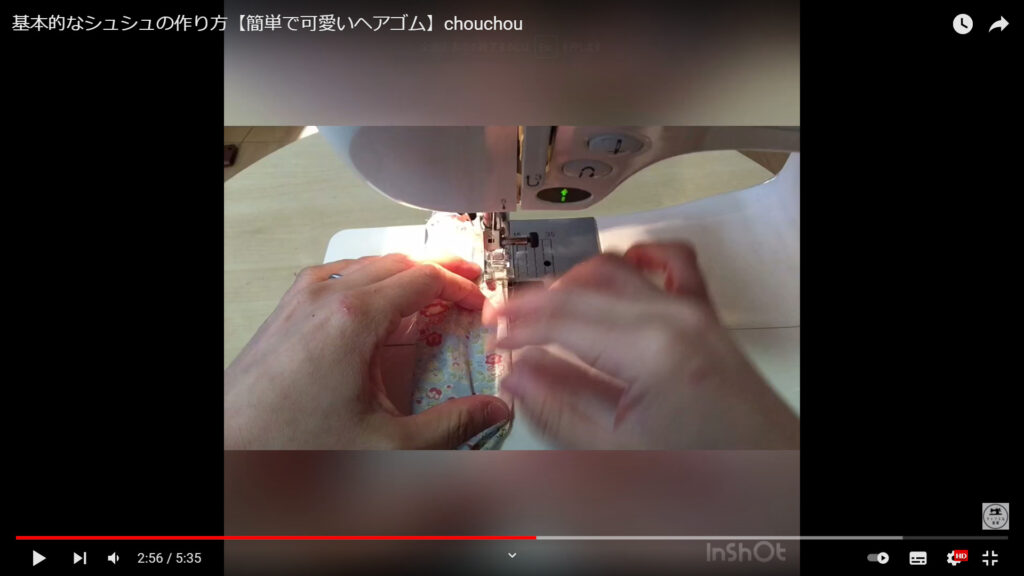 折った布をミシンで縫っていながら内側の布を引っ張る作業を解説している動画で、手で布を押さえながらミシンで縫っている様子。