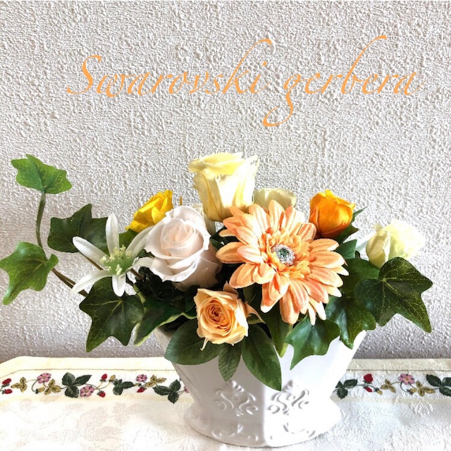 オレンジのガーベラや黄色いバラなどが活けられているフラワーアレジメントが写っている写真。