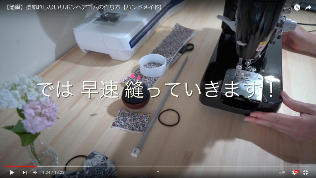 ミシンで縫う作業を解説している動画で、「では早速縫っていきます！」という文と共に、机の上のミシンに手をかけている画像。
