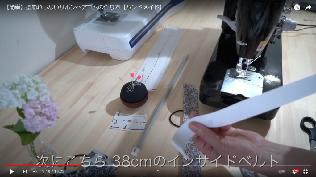 インサイドベルトに切り込みを入れる作業を解説している動画で、インサイドベルトを手に取り、「次にこちら38㎝のインサイドベルト」という文字が表示された画像。