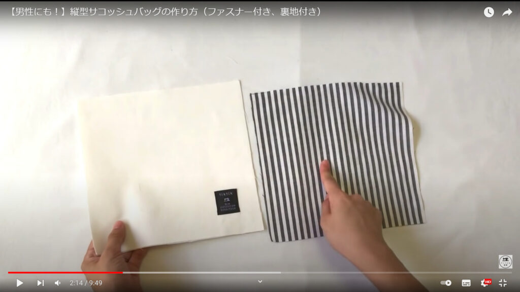 サコッシュの作り方で、外ポケットを作る作業を解説している動画で、机の上に置かれたポケットの表地を手に持ち、裏地を指さしている画像。
