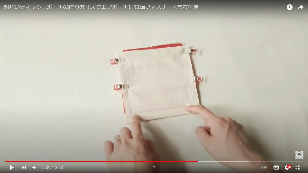ポーチ本体のマチの部分を作る作業を解説している動画で、裏になったポーチの下の部分を指で指した画像。