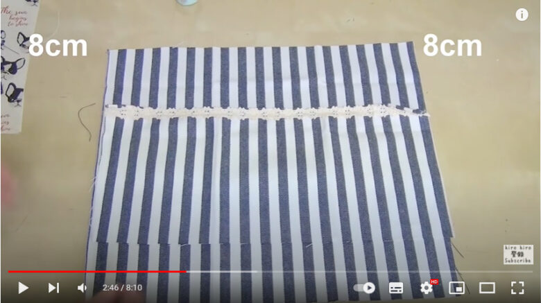 カットクロスの上に、ポケットとなる布を上から8センチの所に重ねている様子。上からの寸法を示す8cmの表示が、重ねられた布の両側に表示されている