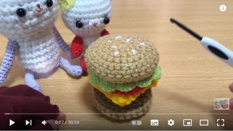 かぎ針で編んだハンバーガーの完成品が中心にあり、左後ろにくまの編みぐるみがふたつ置いてある画像