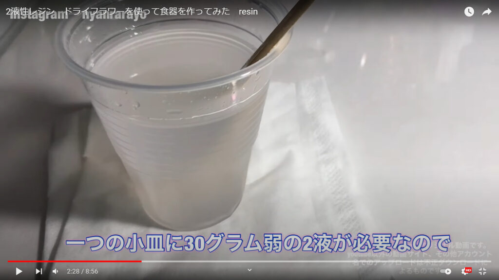 レジンで小皿を作り方の中の混合液を作る作業を解説している動画で、机に置かれた混合液と共に、「一つの小皿に30gグラム弱の2液が必要なので」という文が表示された画像。