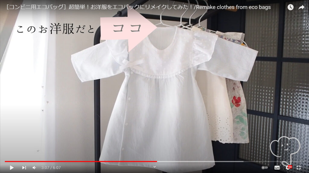 エコバッグに縫い付けるバイアステープを解説している動画で、ハンガーにかけられた白い半そでブラウスの襟元を指す矢印に「このお洋服だとココ」という文字が表示された画像。