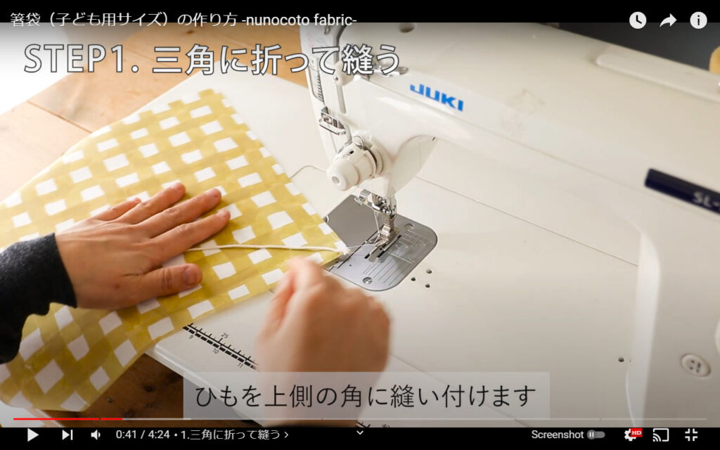 紐を布にミシンで縫いつけている写真です。左手で布を押さえています。