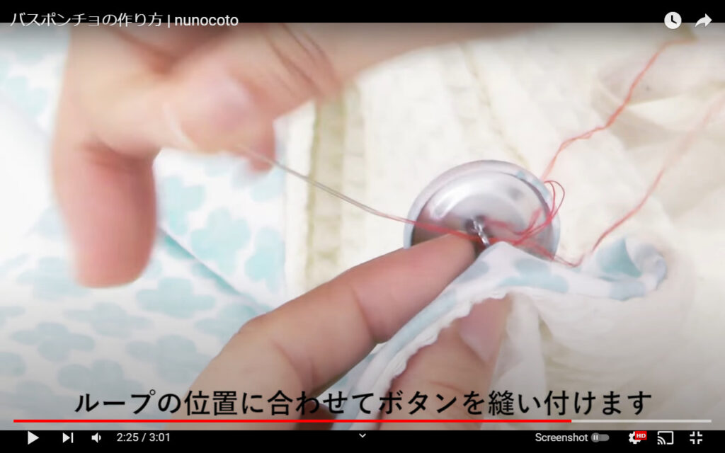 ボタンをバスポンチョ本体に縫いつけている写真です。赤色の糸を使っていて、縫い方や針の動かし方などが確認しやすいですよ。