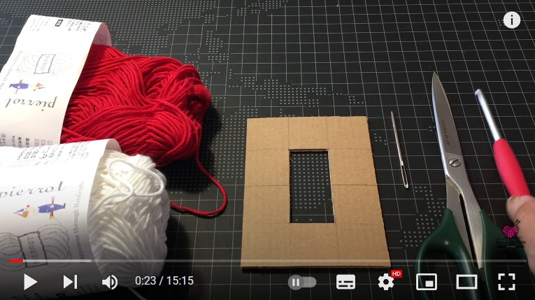 タッセルを作るのに必要な赤い糸、白い糸、タッセルを作るための段ボール板、針、はさみ、かぎ針が並んでいます。