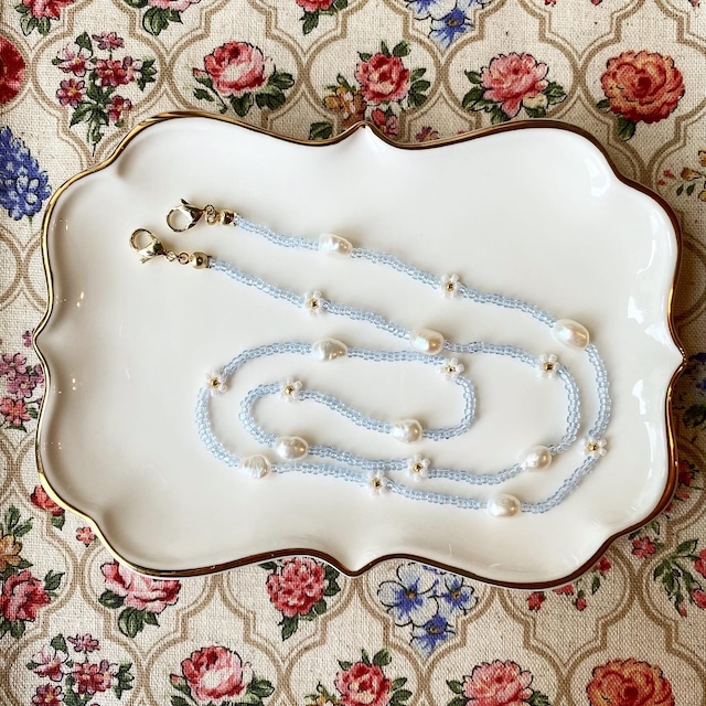 クリアブルーのビーズと白い淡水パールを繋げたネックレスが陶器の皿の上に乗せられている写真。