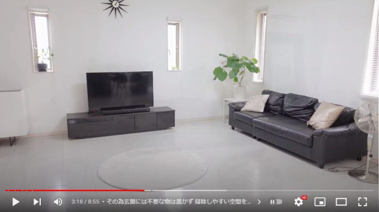 白い壁と床のリビングに黒を基調としたテレビ台やソファーが置かれている様子。
床には白くて丸いラグ以外何も置かれていない。