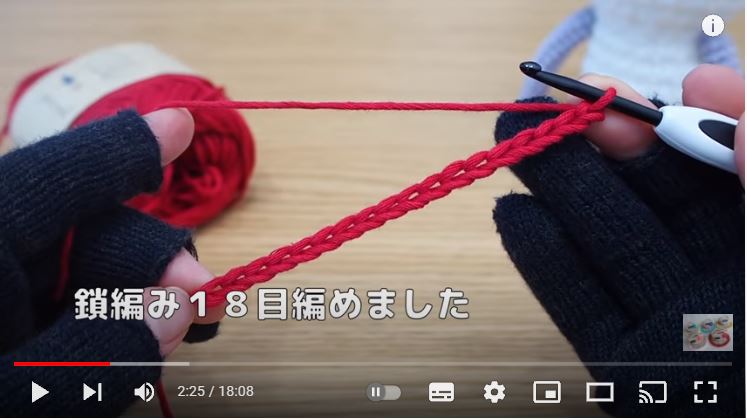 黒い手袋をした両手で赤色のコットン糸でくさり編みを18目編んだところを見せている画像