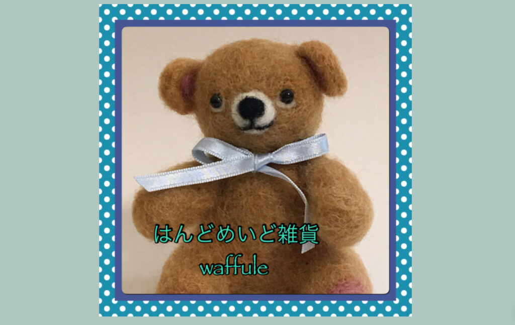 水色のリボンを首に巻いた羊毛フェルトのくまがいる、井村恵子さんのウェブショップ「はんどめいど雑貨 waffule」のトップ画像です。