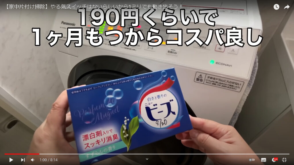 ドラム洗濯乾燥機の前で、青い箱に入った愛用の洗剤、とそのコスパの良さを紹介している様子です。
