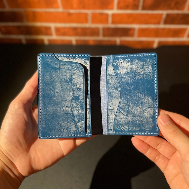 青色の名刺入れを両手で開いている画像。左右それぞれにポケットが2つずつ付いているデザインで、皮には擦れたような模様が入っている。