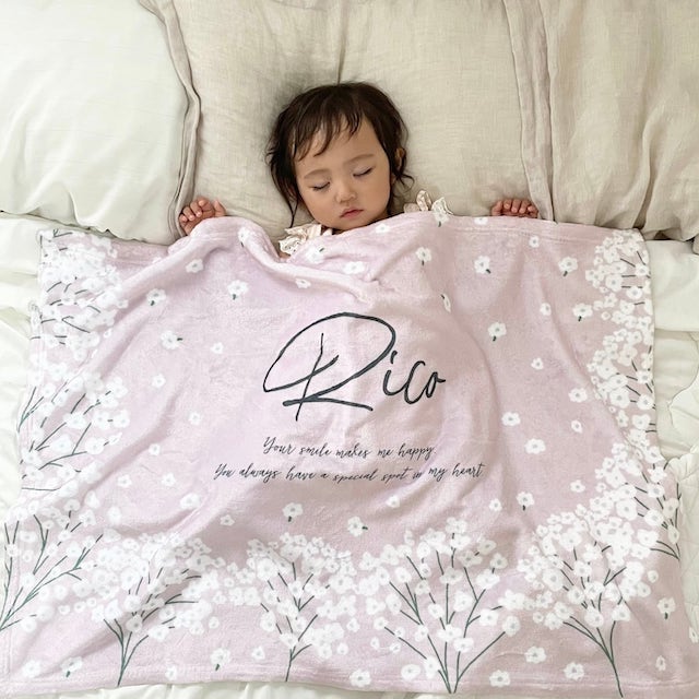 かすみ草柄が描かれた、ピンクのブランケットの画像です。赤ちゃんが気持ちよさそうに寝ています。