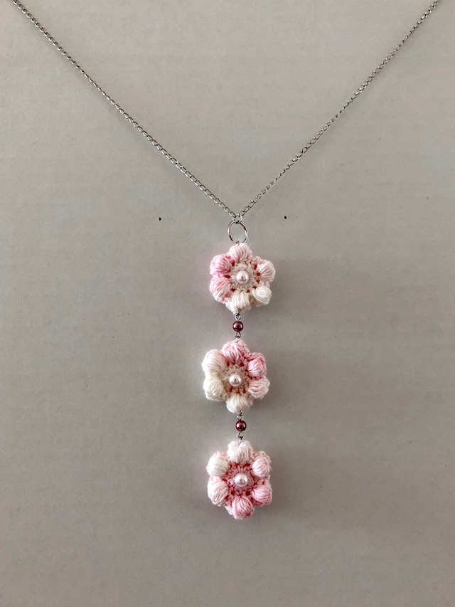 白からピンクにグラデーションで変化しているレース糸で作った花のモチーフが3つ連なったネックレスが写った写真。