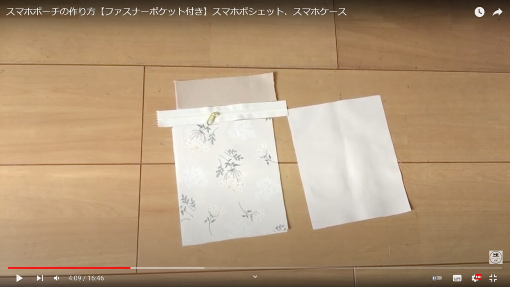 ファスナーを縫い付ける作業を解説している動画で、表地、ファスナー、裏地、ポケットの内生地が机の上に置かれた画像。