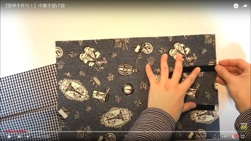 表布の上部に持ち手を縫い付ける作業を解説している動画で、表布の上で持ち手の縫い付けるために配置している様子を表示した画像。